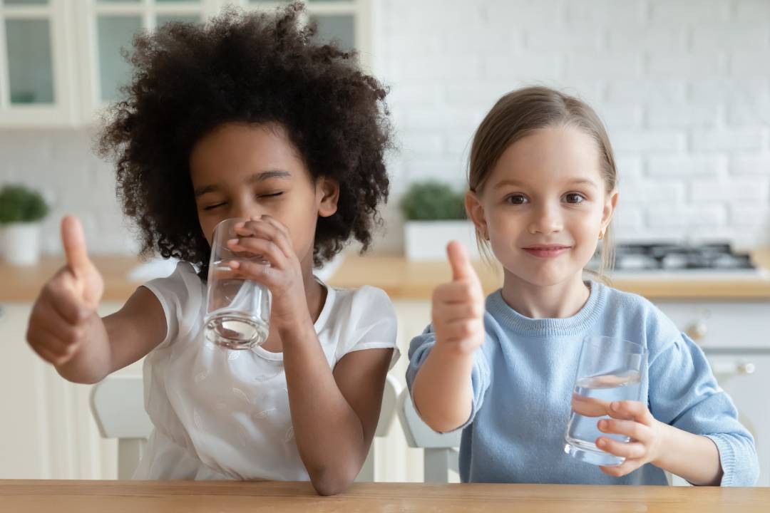 Zwei Mädchen trinken Wasser und strecken den Daumen nach oben