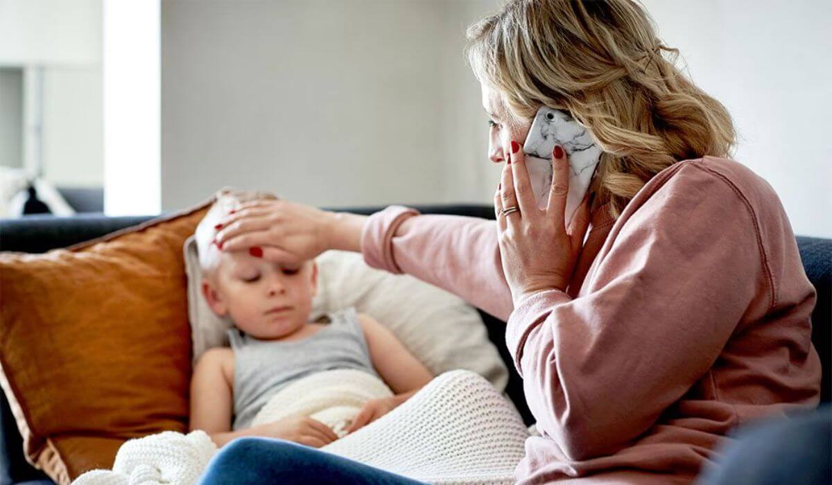 Mutter kümmert sich um krankes Kind auf dem Sofa und fühlt die Stirn – Erkältung oder Fieber bei Kindern