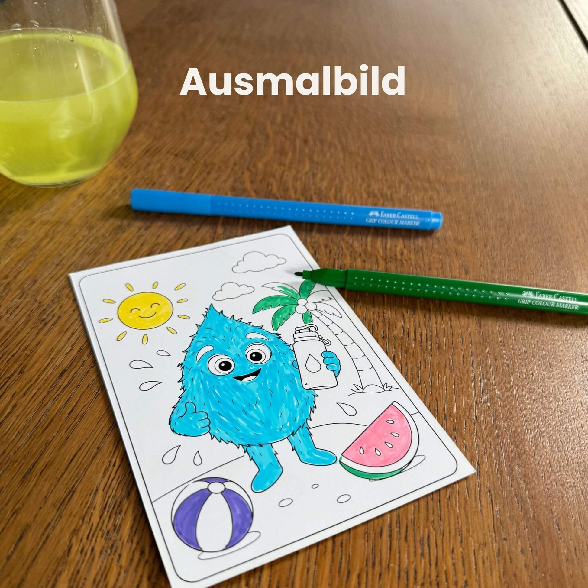 Ausgemaltes Gerol-Ausmalbild mit Buntstiften auf Holztisch, gelbes Elektrolyte-Glas daneben, Sommermotiv mit Sonne und Wassermelone